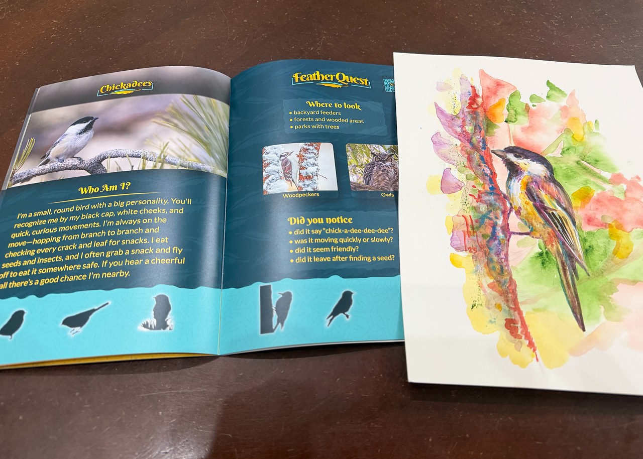 FeatherQuest Discovery book open next to a colorful watercolor painting of a bird