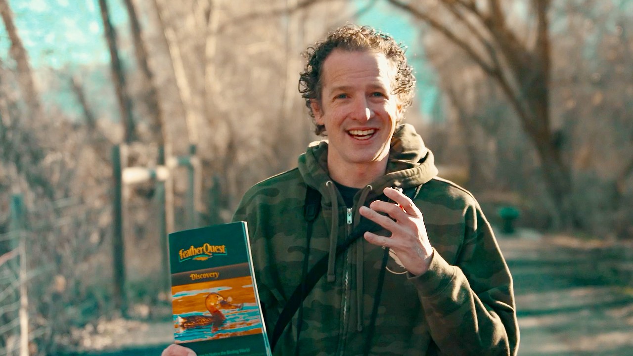 Mike Marshall on a trail holding the FeatherQuest Discovery book during the introduction video