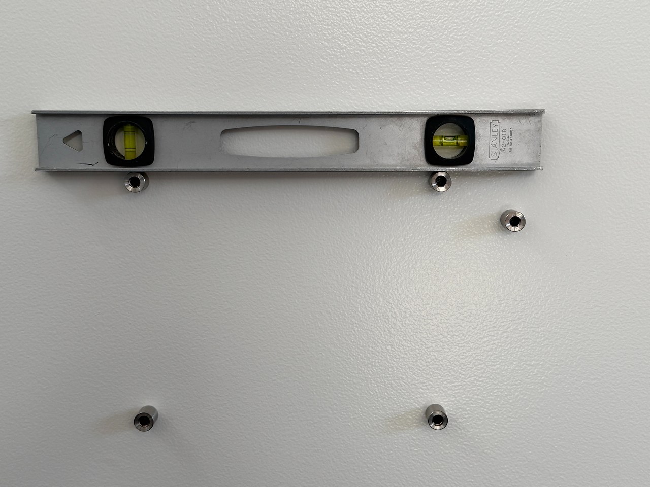 Bubble level resting on wall-mounted standoff bolts to ensure floating acrylic frame hardware is perfectly level