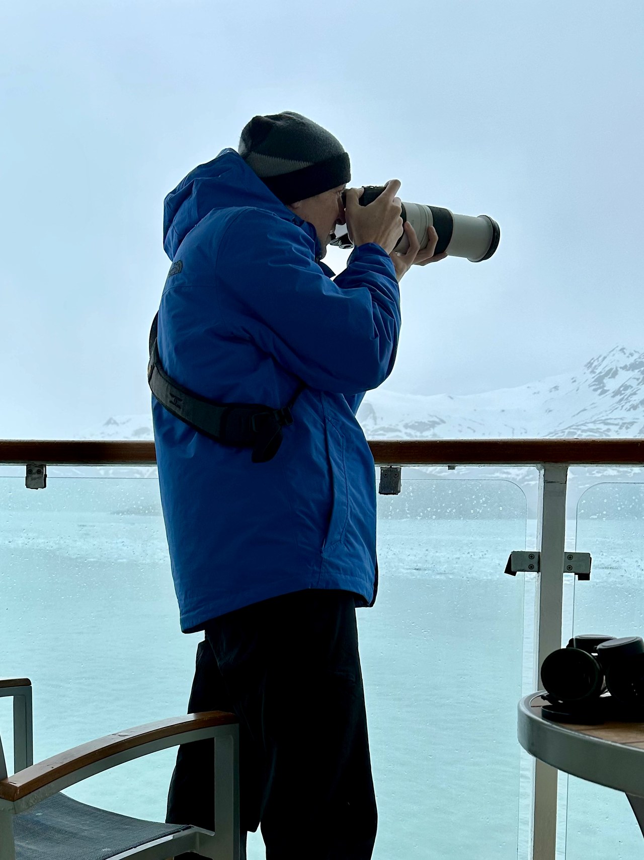 Photographer bundled in cold weather taking photos from a ship balcony in Alaska