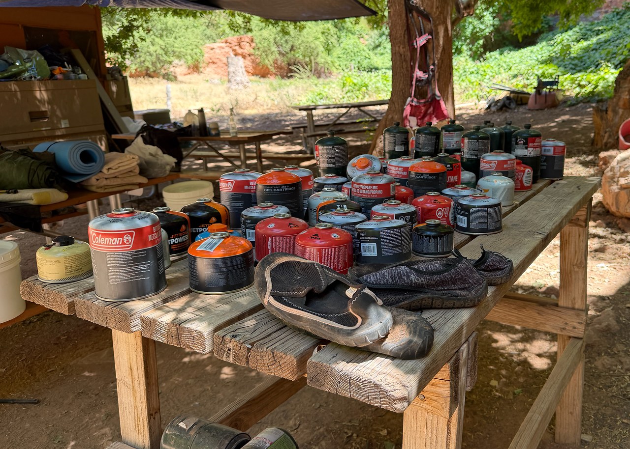 A campground table in Havasupai covered with leftover fuel canisters, water shoes, and abandoned camping supplies.