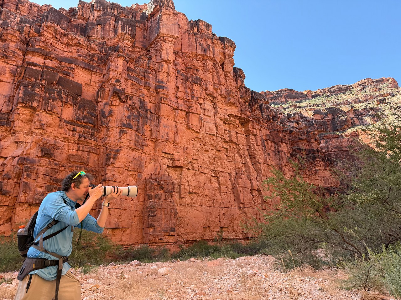 Mike photographing birds with a large telephoto lens beneath red canyon walls in Havasupai.