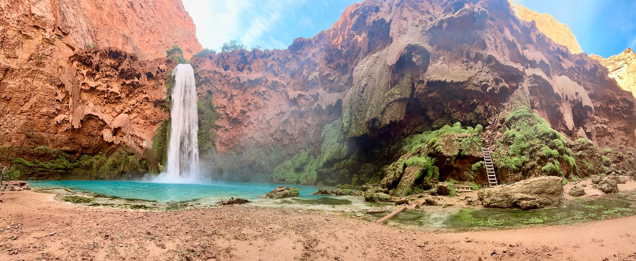 Ultra-wide panorama of Mooney Falls with its turquoise pool, travertine cliffs, chains, and ladders.