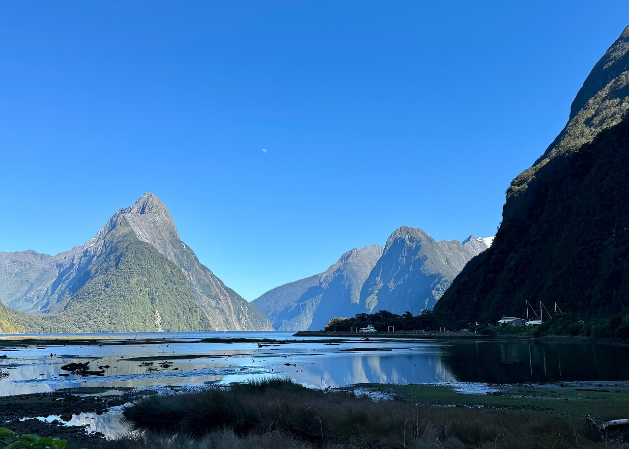 Final morning view across the still harbor of Milford Sound with Mitre Peak and the surrounding mountains reflected in the water