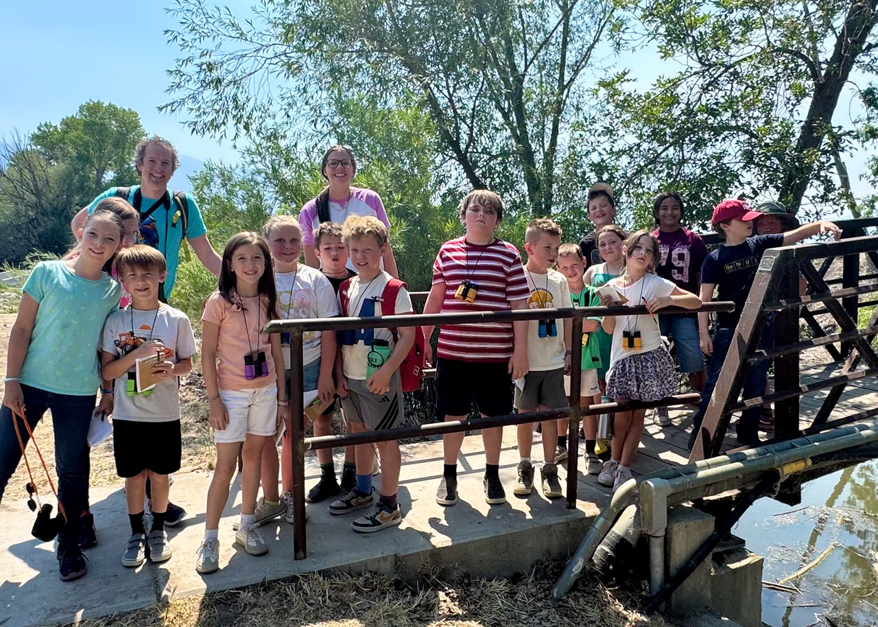 Nature school campers and teachers standing with binoculars on a bridge during a FeatherQuest bird walk
