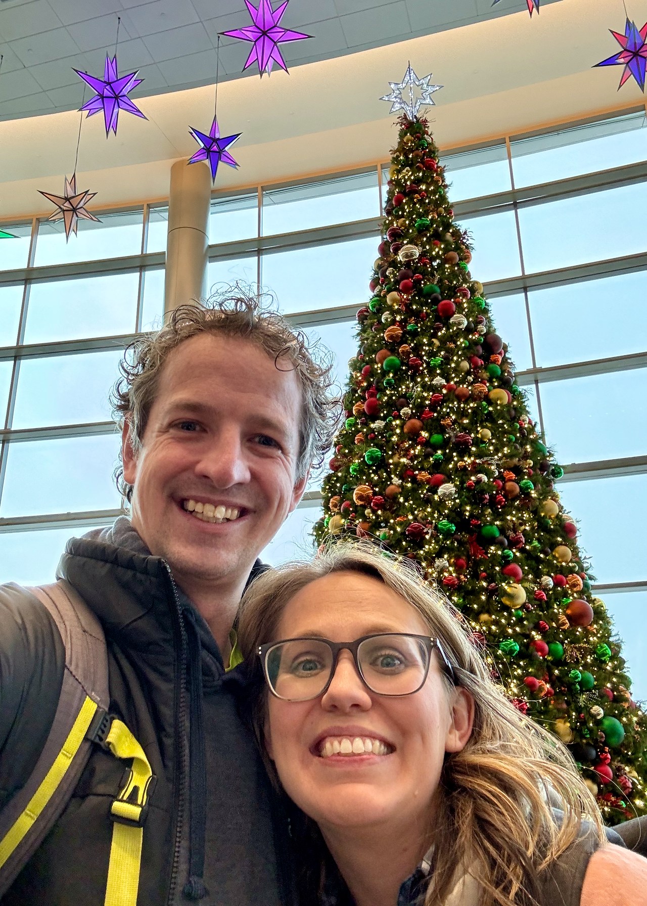 Mike and his wife smiling by a Christmas tree at the Salt Lake City airport before leaving for New Zealand