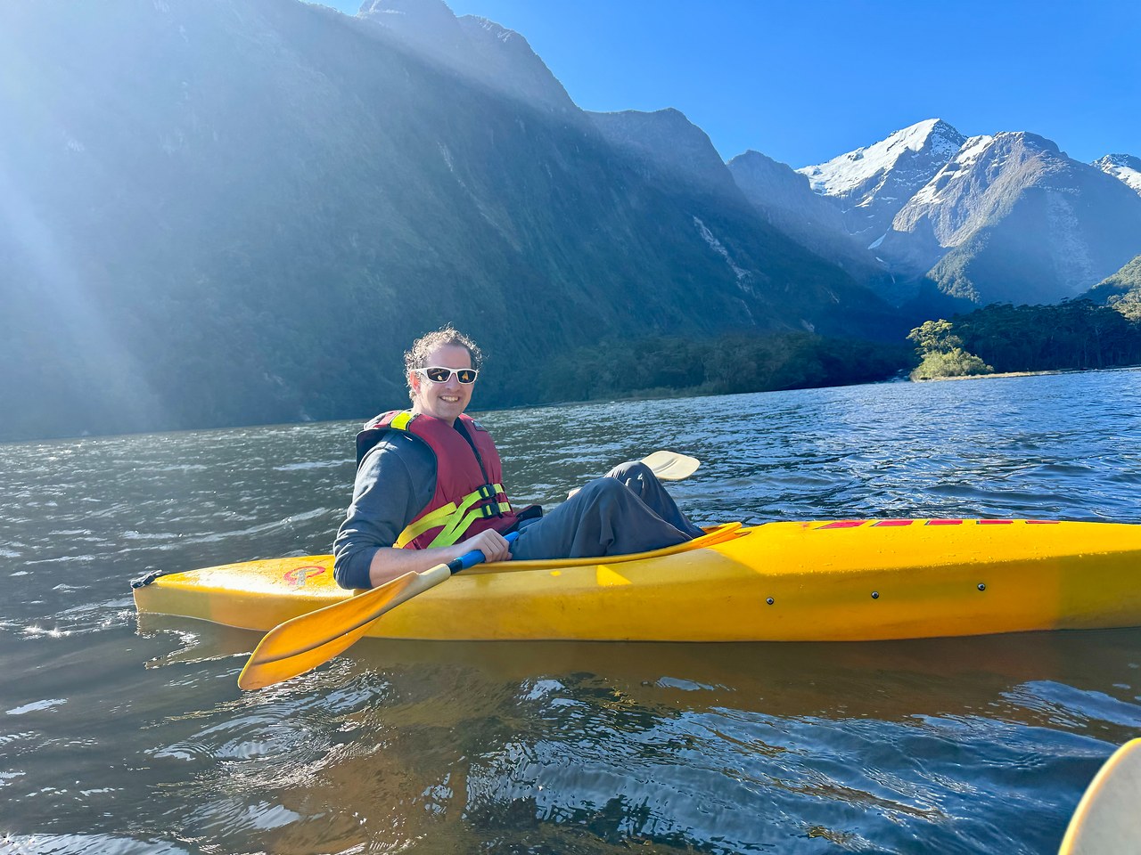 Kayaking beneath towering mountains and waterfalls in Milford Sound under clear skies