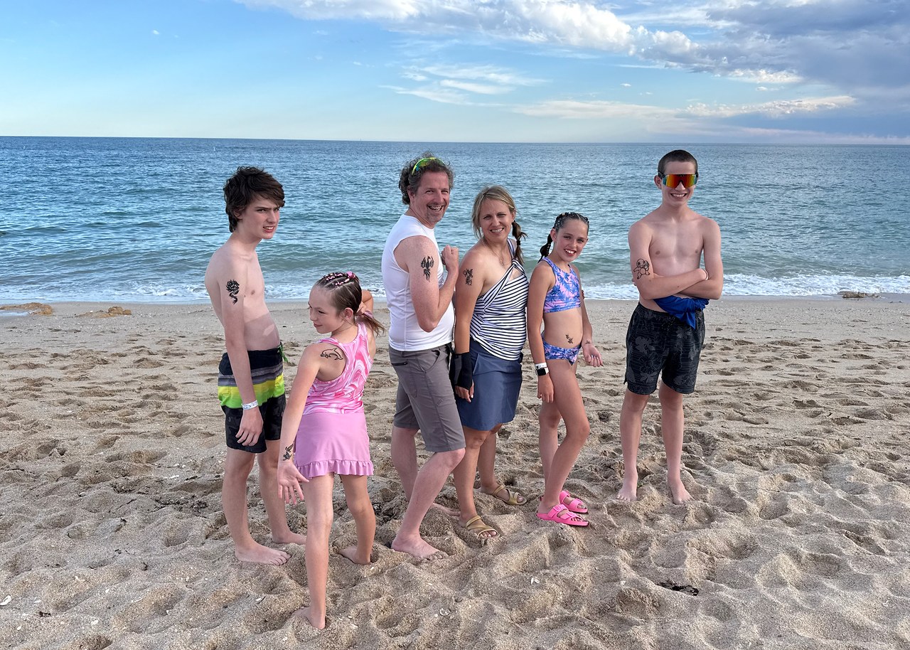 Mike and Stacy standing with their four kids on the beach in Puerto Peñasco, showing off their henna tattoos with the Sea of Cortez behind them