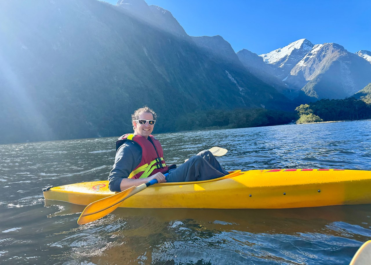 Kayaking beneath steep mountain walls in Milford Sound during evening light