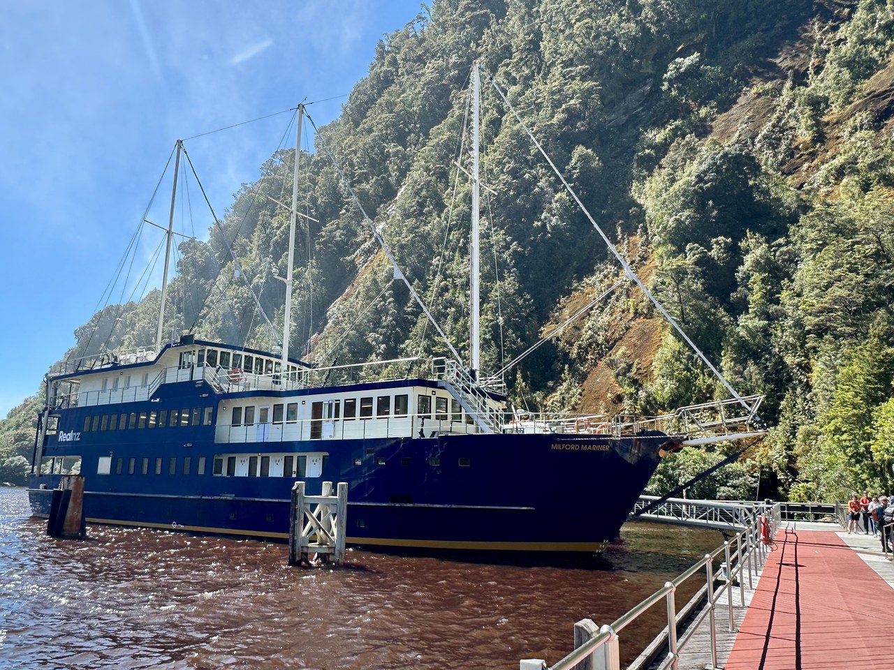 The Milford Mariner overnight cruise ship docked beneath steep forested cliffs in Milford Sound