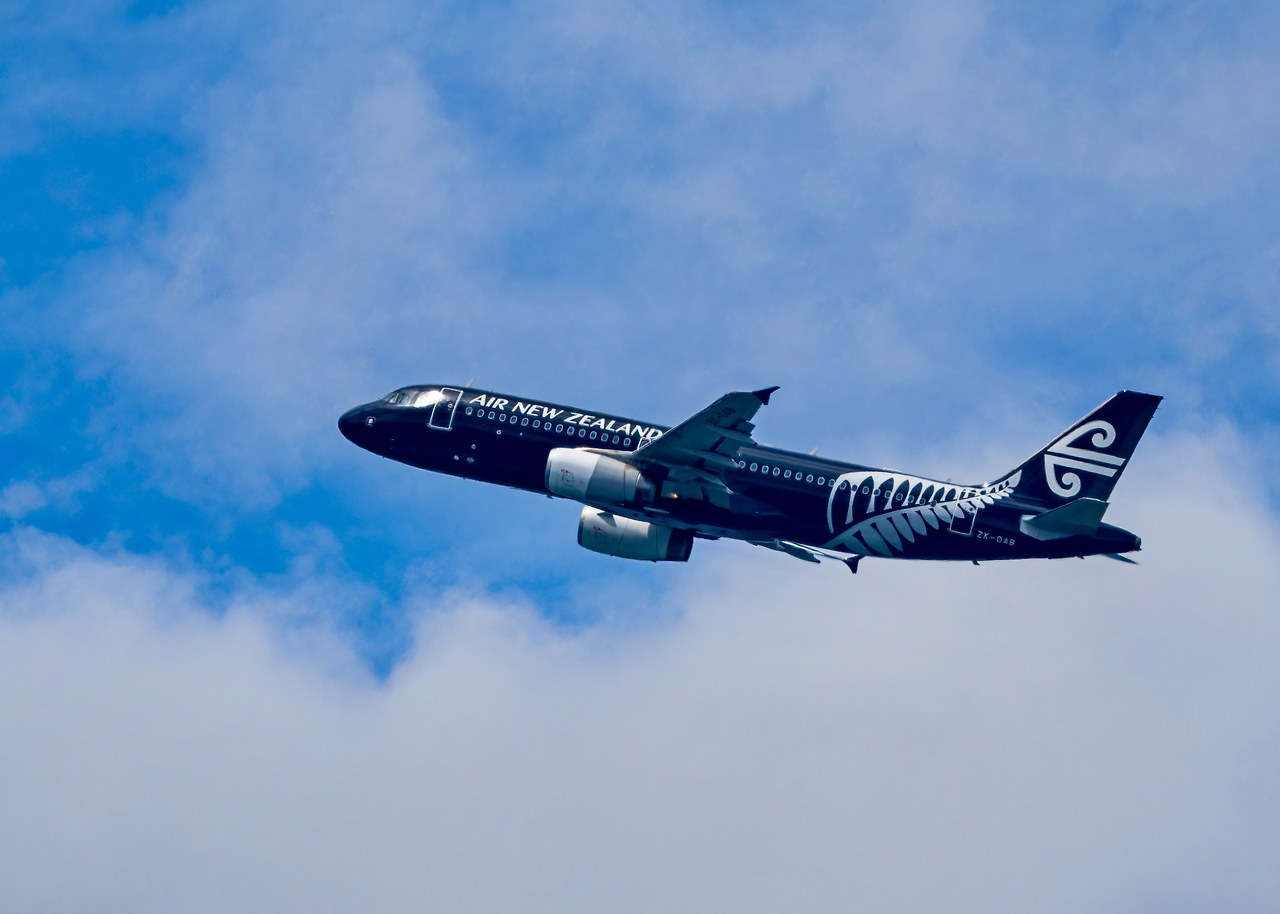 Air New Zealand aircraft climbing through scattered clouds after departure from Auckland, New Zealand.