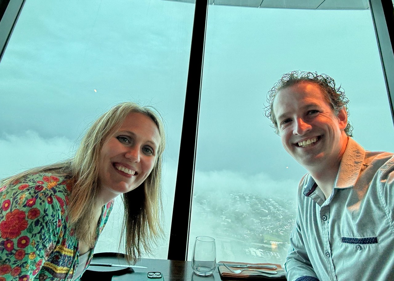 Mike and Stacy smiling together at dinner beside the windows high inside Auckland's Sky Tower.