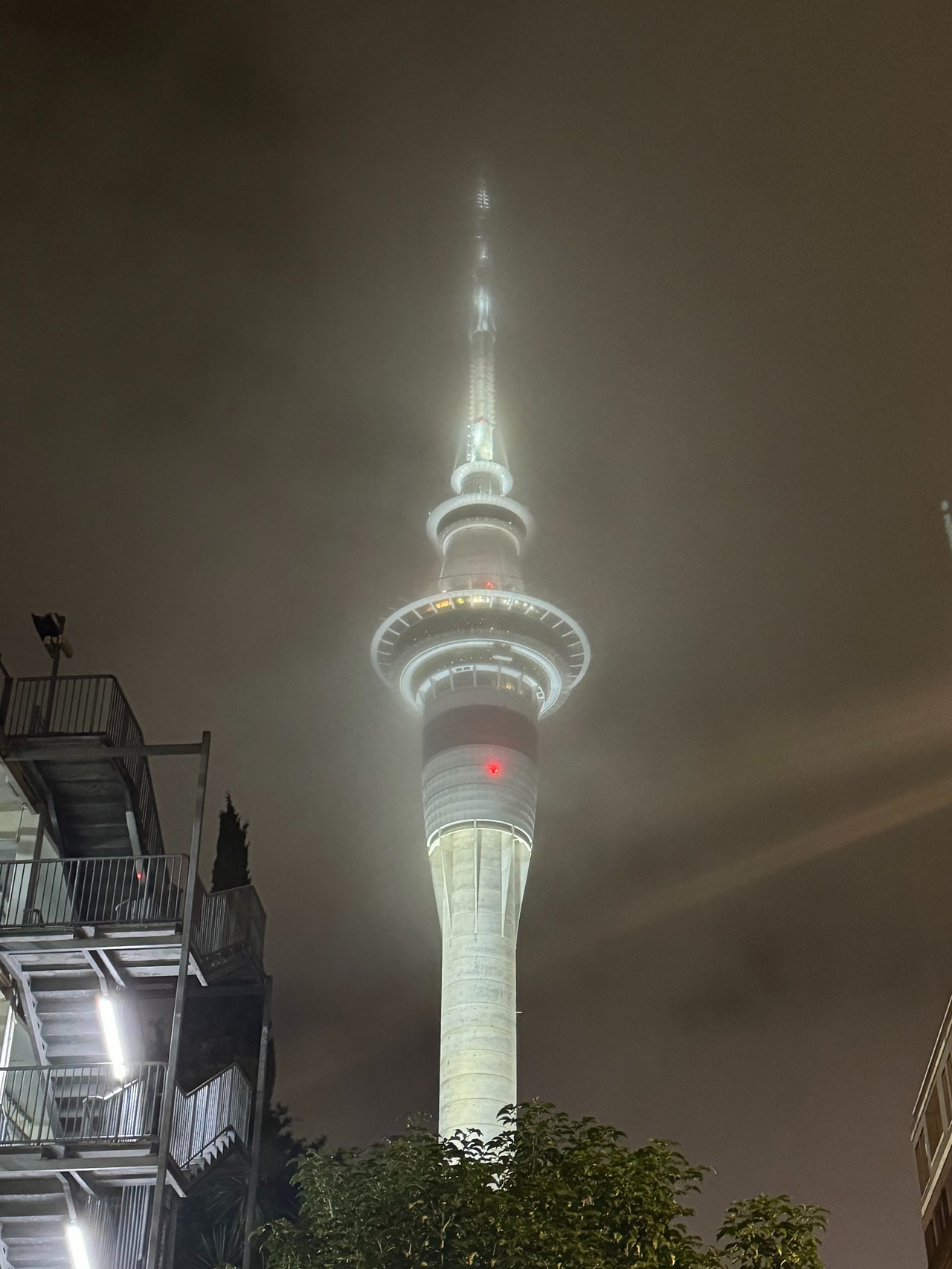 Auckland Sky Tower glowing through low clouds and fog at night.
