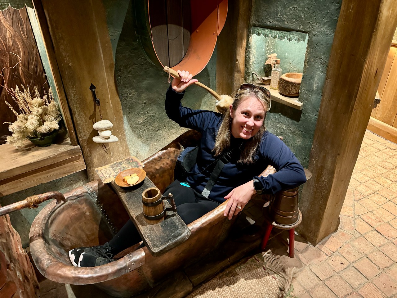 Stacy playfully posing inside a bathtub in a furnished hobbit hole.
