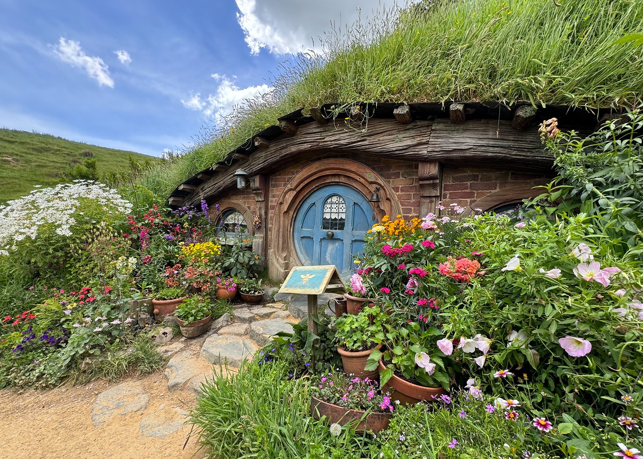 Blue-doored hobbit hole surrounded by flowers and greenery at Hobbiton.