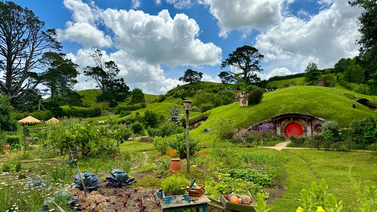 Vibrant vegetable gardens and a red-doored hobbit hole beneath green hills at the Hobbiton Movie Set in New Zealand.