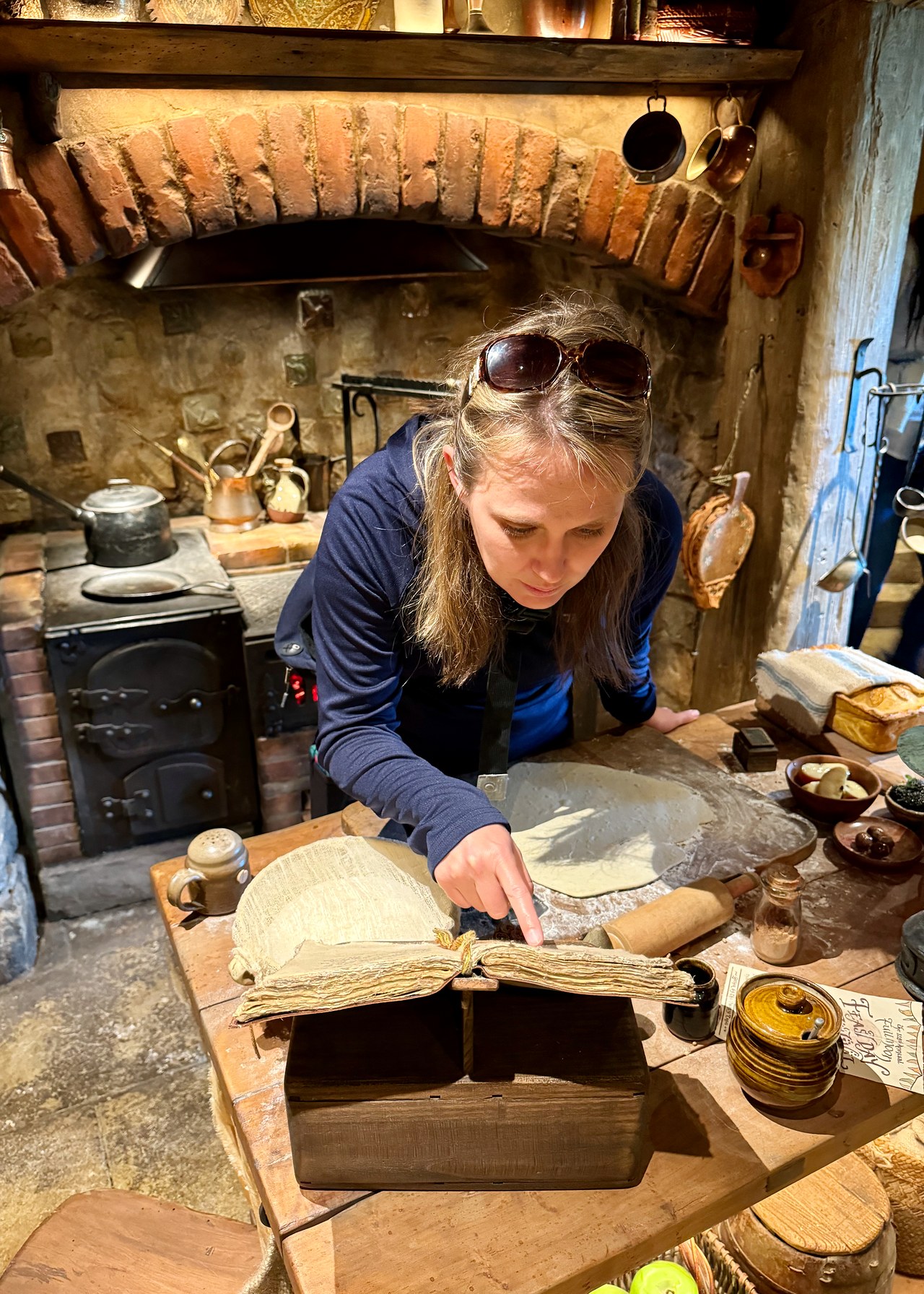 Hearth, kitchen tools, and shelves inside a furnished Hobbiton home.