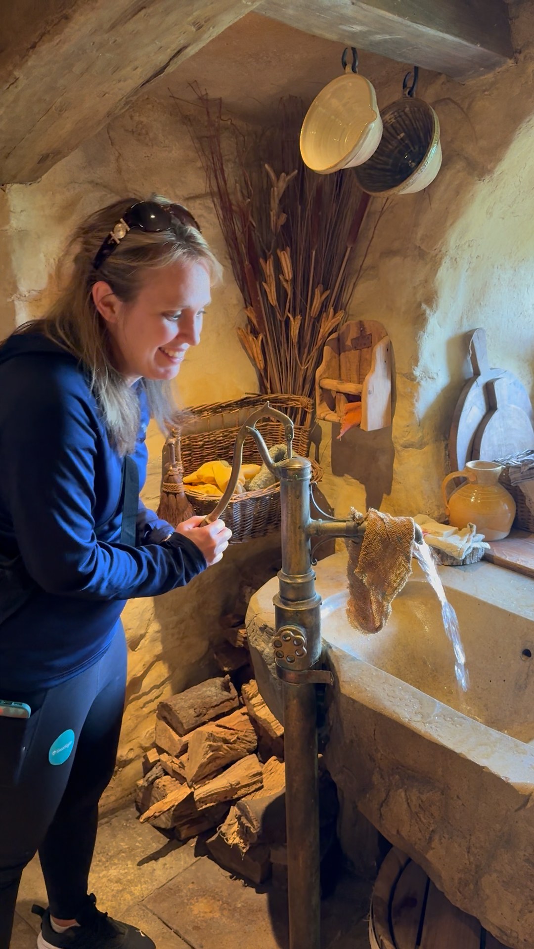 Stacy operating a working water pump inside the kitchen of a furnished hobbit hole at Hobbiton.