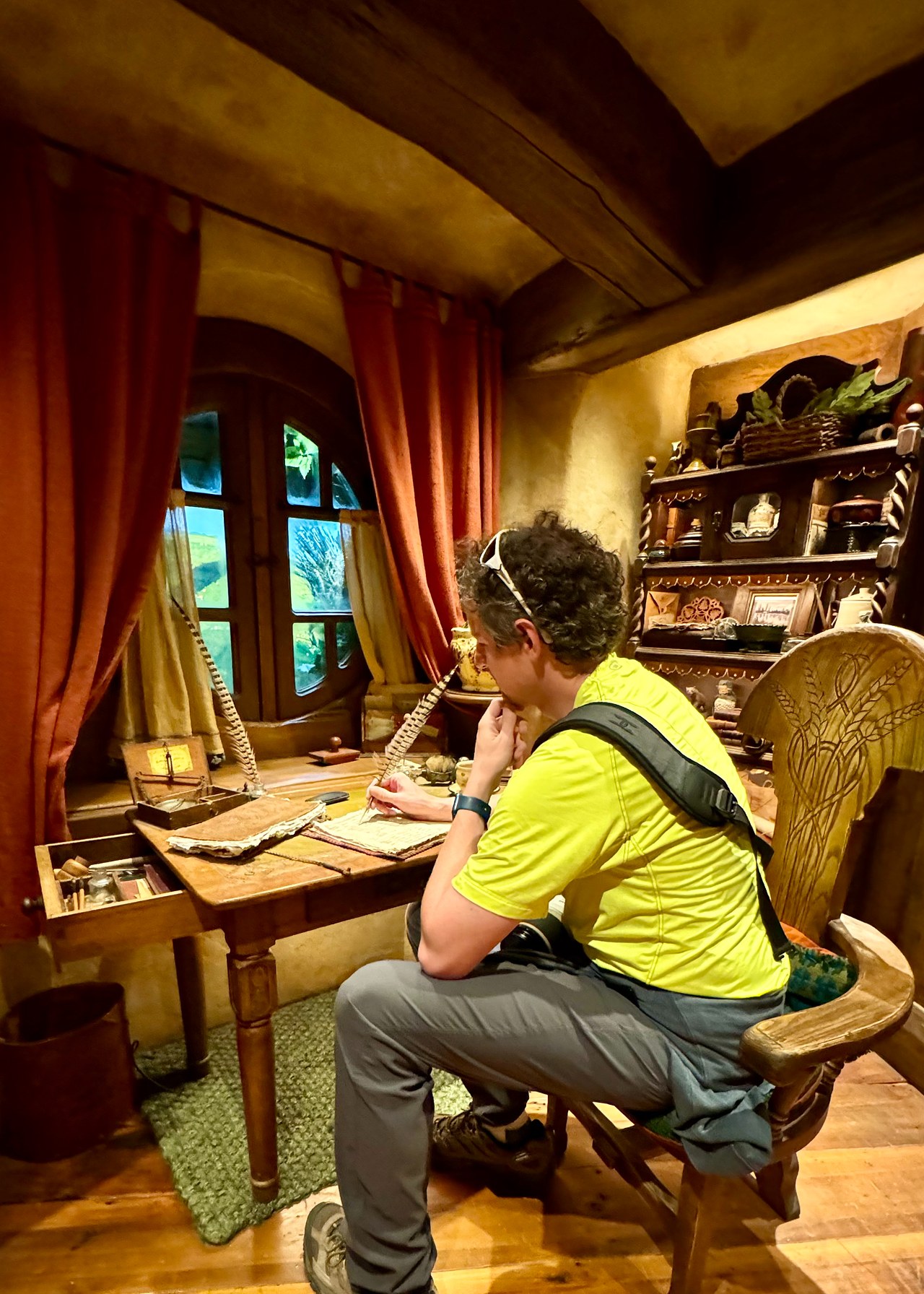 Mike sitting at a writing desk inside a fully furnished hobbit hole at Hobbiton.