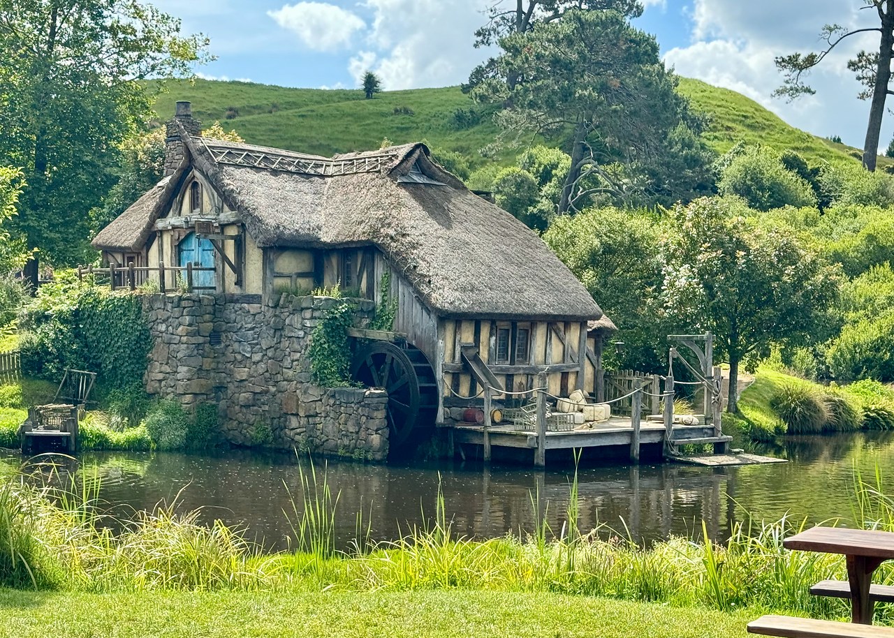 Hobbiton watermill beside the pond under a bright sky.