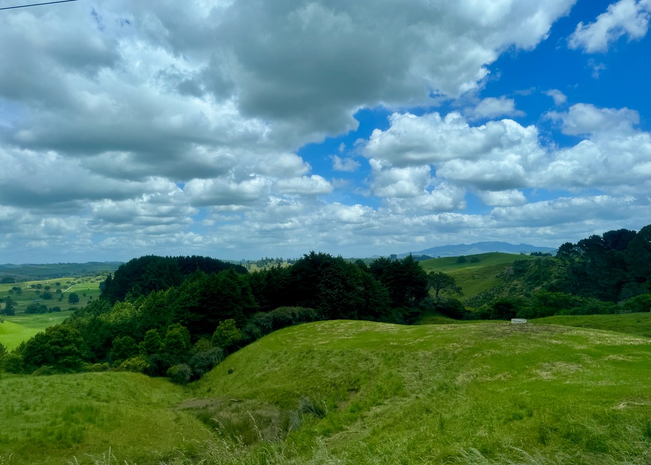 Rolling green farmland and dramatic clouds seen from the coach while crossing the Waikato region of New Zealand.