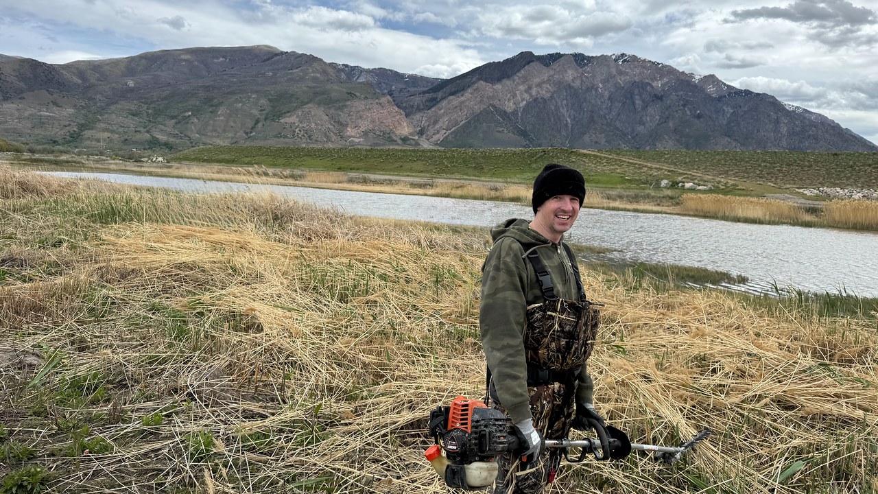 Mike standing in waders with a brush cutter during a phragmites removal project in Utah marsh habitat
