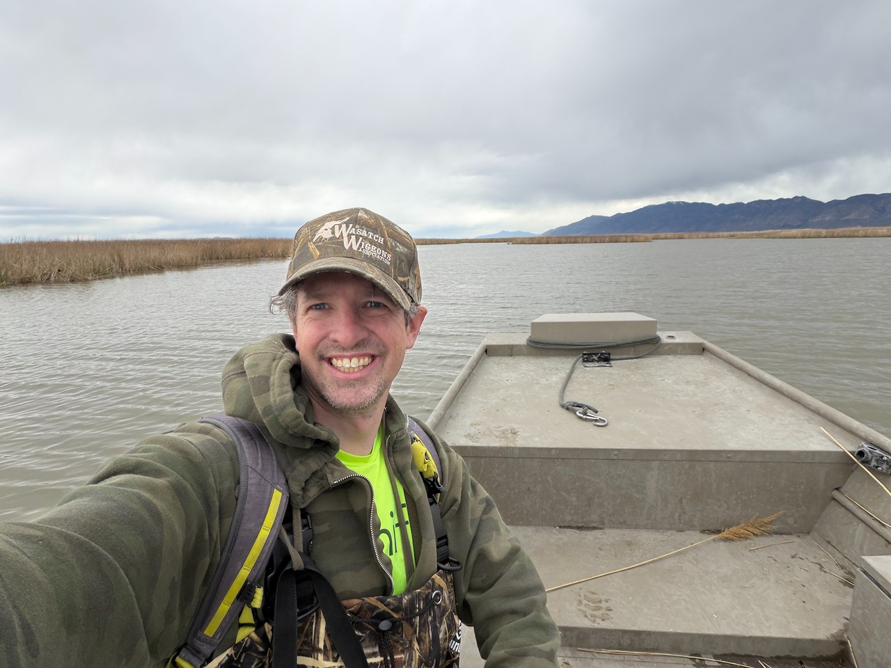 Mike Marshall standing in a marsh boat at Willard Bay wearing a Wasatch Wigeons hat after a habitat restoration workday
