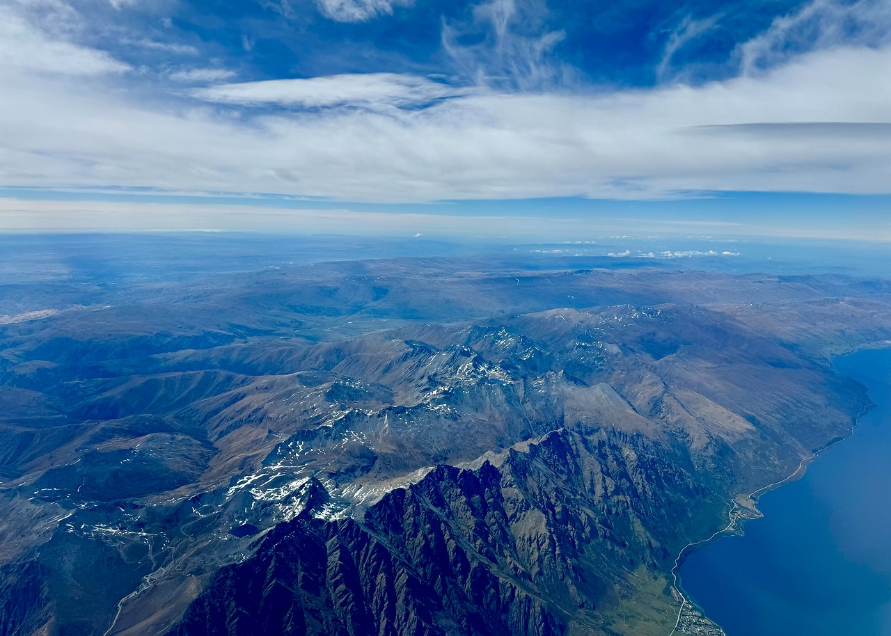 Aerial view of rugged Southern Alps ridges and blue lake water during the flight from Queenstown to Wellington.