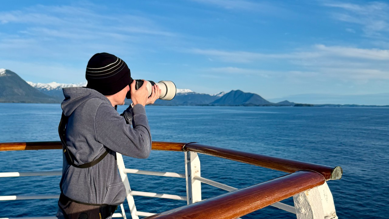Mike Marshall photographing wildlife from an Alaska cruise ship, representing the curiosity and observation behind FeatherQuest Stories